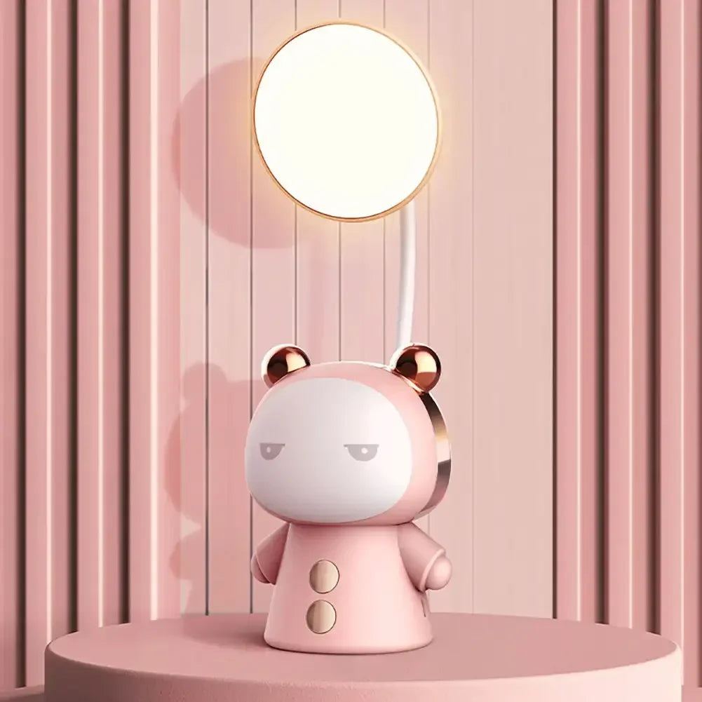 Lampe de bureau enfant Câlin rose, lumière du haut allumée, sur un socle rond devant un mur à lattes roses