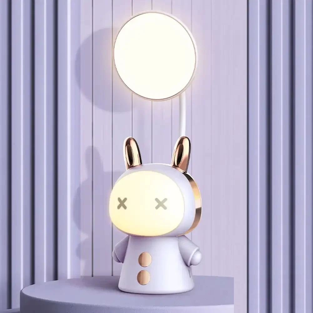 Lampe de bureau enfant Câlin violet, lumière du haut allumée, sur un socle rond devant un mur à lattes violet pâle