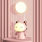 Lampe de bureau enfant Câlin rose, lumière du haut et visage allumés, sur un socle rond devant un mur à lattes roses