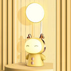 Lampe de bureau enfant Câlin jaune, lumière du haut et visage allumés, sur un socle rond devant un mur à lattes jaunes
