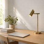 Lampe de bureau Auria en laiton allumée sur un bureau en chêne le jour, décor Japandi