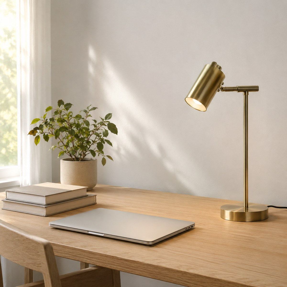 Lampe de bureau Auria en laiton allumée sur un bureau en chêne le jour, décor Japandi