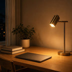 Lampe de bureau Auria en laiton allumée sur un bureau le soir, ambiance chaleureuse