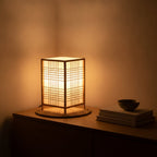 Lampe de bureau design Flora allumée le soir, modèle Croisillon, sur une console en bois clair
