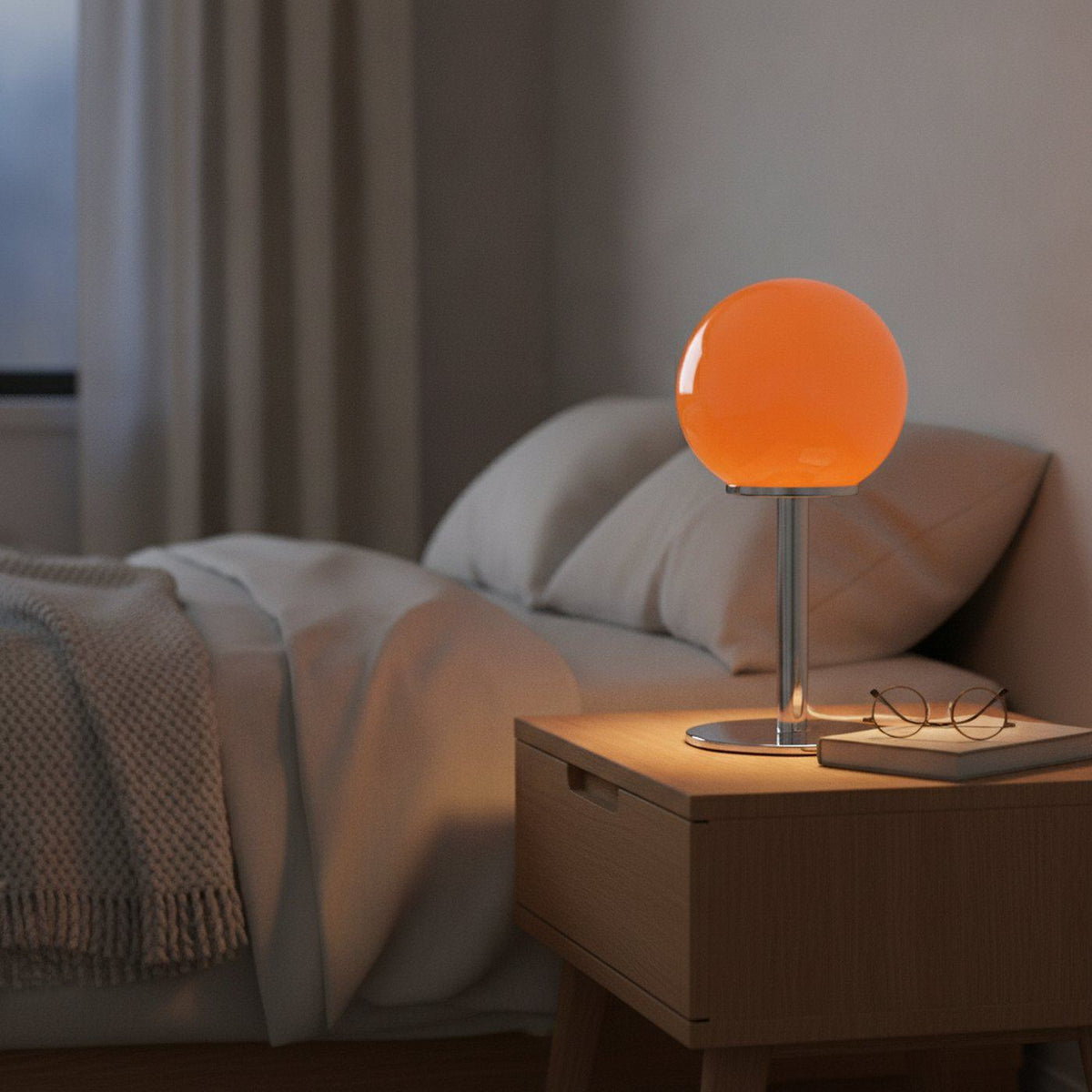 Lampe de bureau design Stellaria, globe en verre orange allumé le soir sur une table de chevet en bois clair