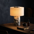 Lampe Vesta en marbre allumée sur un bureau le soir, ambiance feutrée