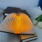Lampe livre Conte allumée sur un lit, posée sur un carnet, à côté de tulipes blanches — Candeora