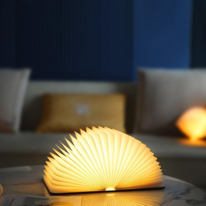 Lampe livre Conte allumée sur une table de salon le soir, lueur chaude — Candeora