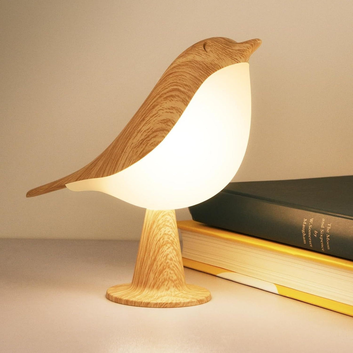 Veilleuse oiseau Piou allumée à côté d'un livre, finition effet bois — Candeora
