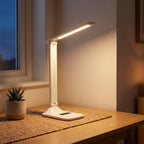 Lampe de bureau LED pliable Aube en lumière chaude sur un bureau en chêne, ambiance du soir