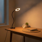 Lampe de bureau LED à pince Véga allumée en teinte chaude sur un bureau, ambiance du soir