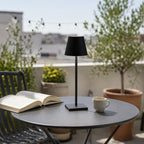 Lampe sans fil Alizé noire sur une table de terrasse, en journée — Candeora