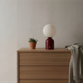 Lampe de bureau sans fil Foehn Candeora coloris rouge, globe opalin, posée sur une commode