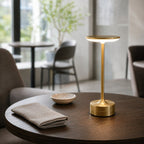 Lampe sans fil Zéphyr finition or allumée sur une table en noyer, en journée — Candeora